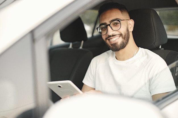 Jovem indiano bonito olhando para a câmera enquanto está sentado no carro. homem vestindo camiseta branca e óculos