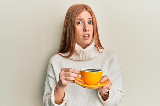 Foto grátis jovem irlandesa bebendo uma xícara de café sem noção e conceito de dúvida de expressão confusa