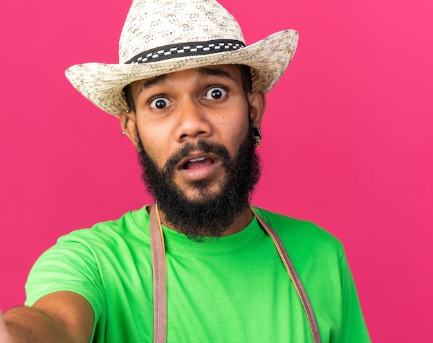 Jovem jardineiro afro-americano assustado com um chapéu de jardinagem segurando uma câmera