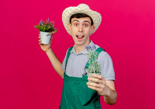 Jovem jardineiro alegre usando chapéu de jardinagem segurando vasos de flores