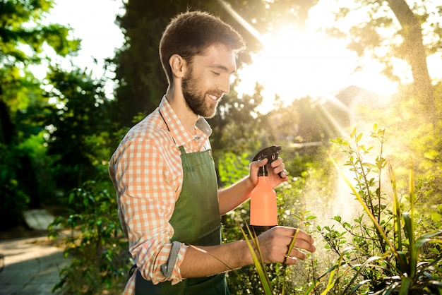 Foto grátis jovem jardineiro bonito sorrindo, regando, cuidando das plantas