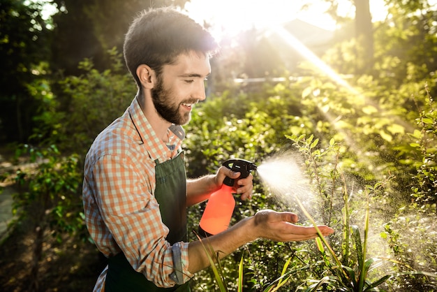 Foto grátis jovem jardineiro bonito sorrindo, regando, cuidando das plantas