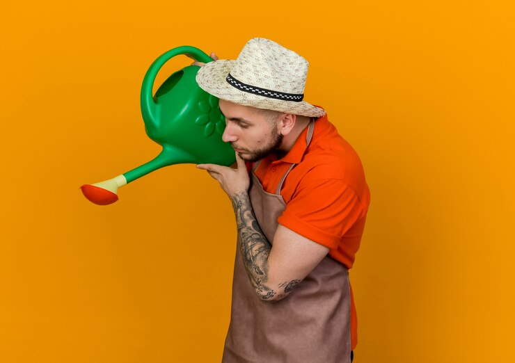 Foto grátis jovem jardineiro com chapéu de jardinagem parado de lado segurando um regador olhando para baixo