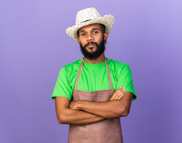 Foto grátis jovem jardineiro confiante afro-americano usando chapéu de jardinagem e cruzando as mãos isoladas na parede azul