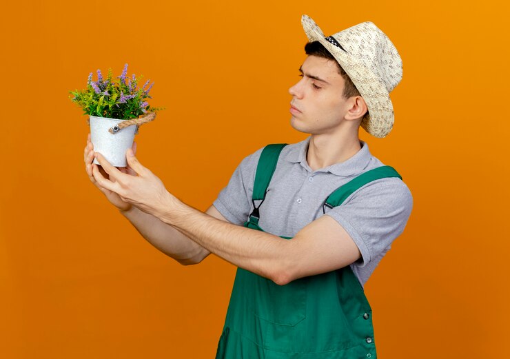 Foto grátis jovem jardineiro confiante com um chapéu de jardinagem segura e olha para as flores