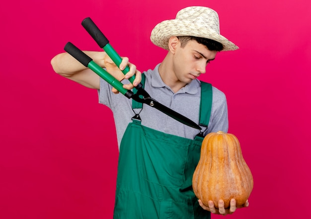 Jovem jardineiro confiante usando chapéu de jardinagem segurando uma tesoura e olhando para uma abóbora