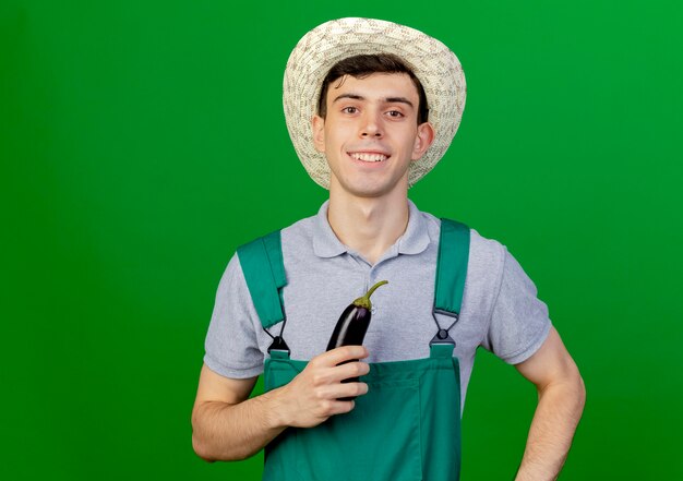 Jovem jardineiro sorridente com chapéu de jardinagem segurando berinjela
