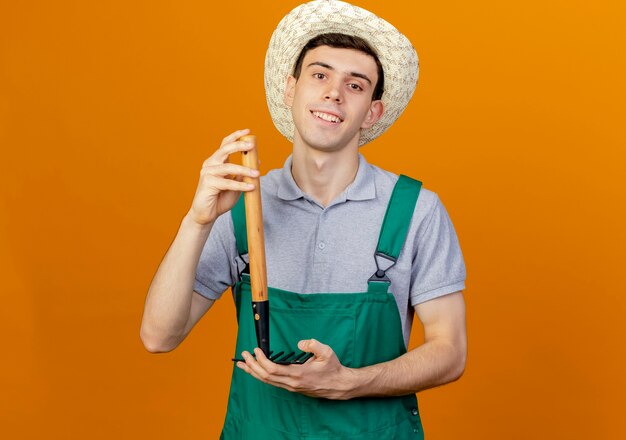 Jovem jardineiro sorridente com chapéu de jardinagem segurando o ancinho de cabeça para baixo