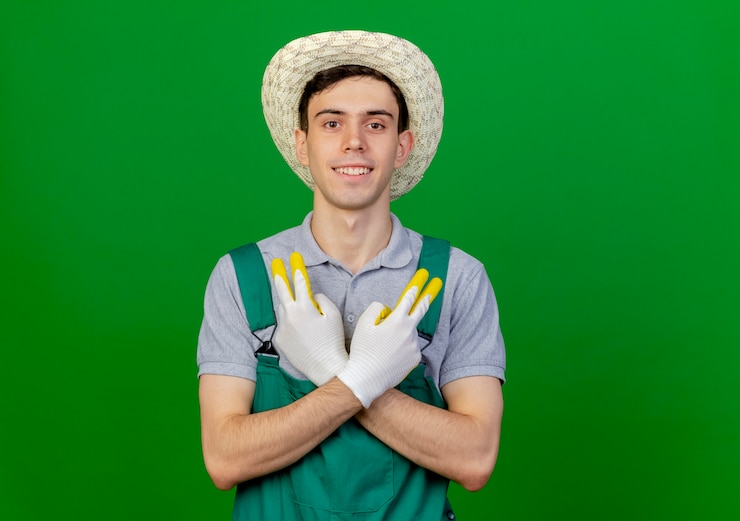 Foto grátis jovem jardineiro sorridente usando luvas e chapéu de jardinagem gesticula sinal de vitória