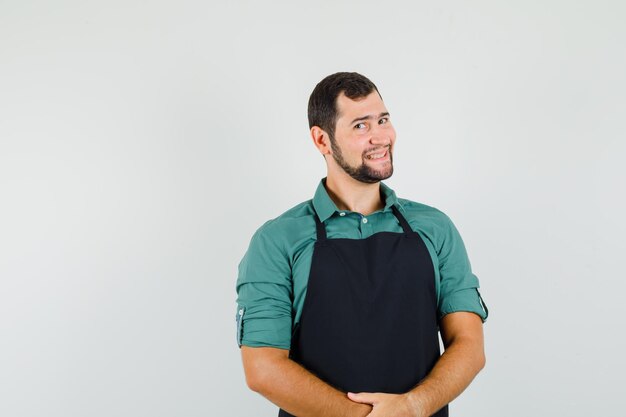 Jovem jardineiro sorrindo em t-shirt, avental e olhando feliz, vista frontal.