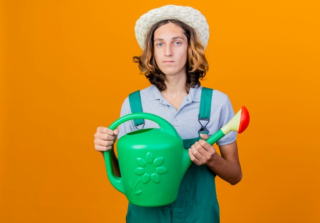 Foto grátis jovem jardineiro vestindo macacão e chapéu segurando um regador