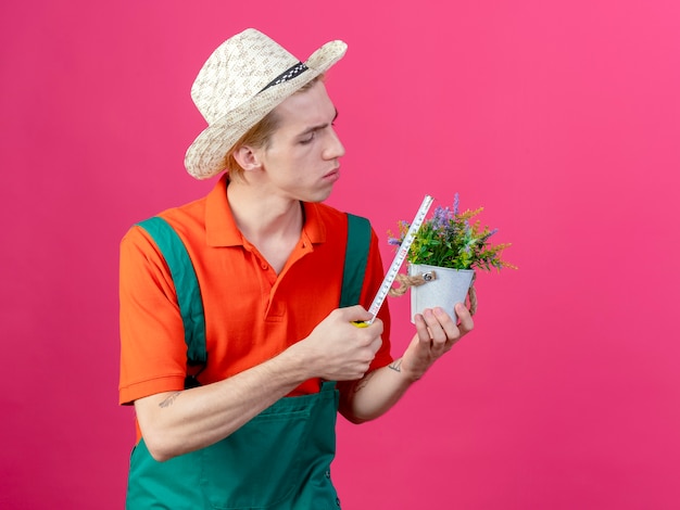 Jovem jardineiro vestindo macacão e chapéu segurando um vaso de planta para medi-lo