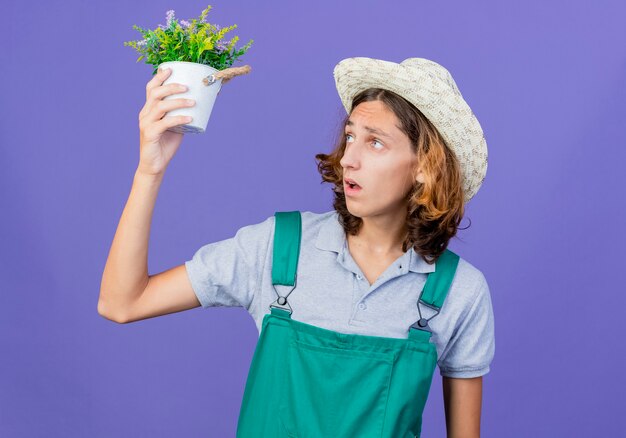 Foto grátis jovem jardineiro vestindo macacão e chapéu segurando um vaso de plantas