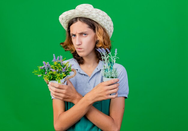 Jovem jardineiro vestindo macacão e chapéu segurando vasos de plantas