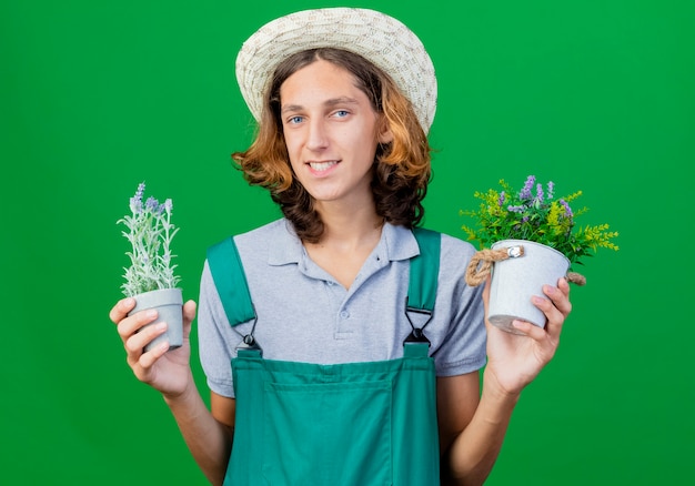 Jovem jardineiro vestindo macacão e chapéu segurando vasos de plantas