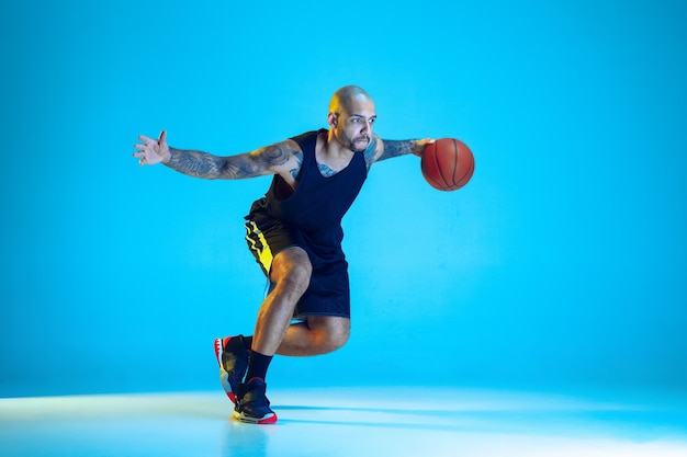 Jovem jogador de basquete do time vestindo roupas esportivas, treinando em ação, isolado na parede azul com luz de néon