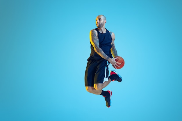 Jovem jogador de basquete do time vestindo roupas esportivas, treinando em ação, movimento na parede azul com luz de néon