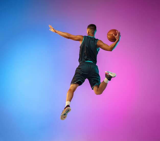 Jovem jogador de basquete em movimento no fundo gradiente do estúdio sob luz de néon