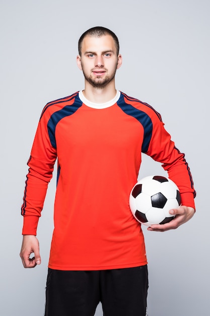 Foto grátis jovem jogador de futebol com a bola nas mãos, vestido com uma camisa vermelha na frente do branco