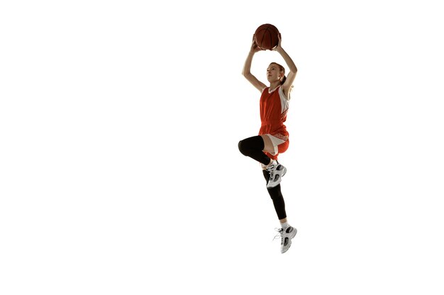 Jovem jogadora de basquete feminino caucasiano em ação, movimento em salto isolado no fundo branco. Garota esportiva Redhair. Conceito de esporte, movimento, energia e estilo de vida dinâmico e saudável. Treinamento.