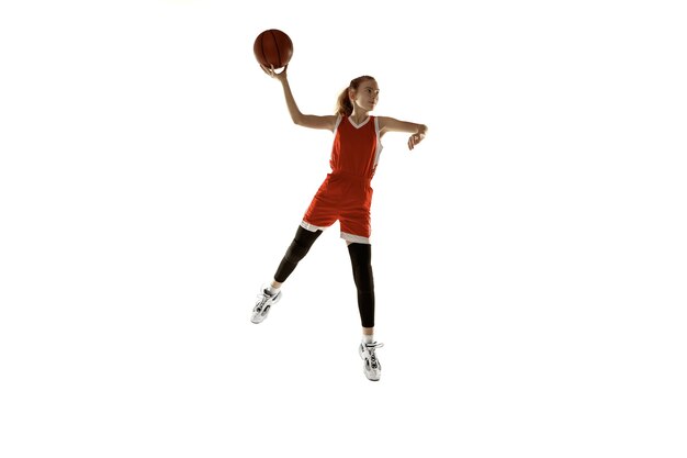 Jovem jogadora de basquete feminino caucasiano em ação, movimento em salto isolado no fundo branco. Garota esportiva Redhair. Conceito de esporte, movimento, energia e estilo de vida dinâmico e saudável. Treinamento.