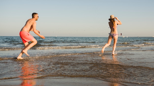 Jovem jogando o esguicho de água sobre sua namorada perto do mar na praia