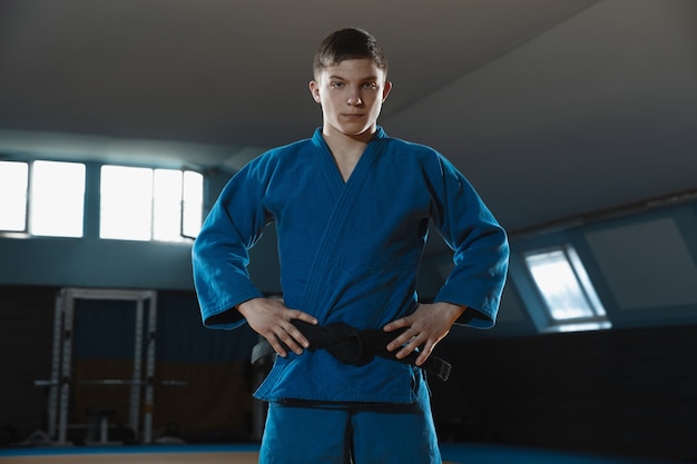 Jovem judoca de quimono posando confiante na academia forte e saudável
