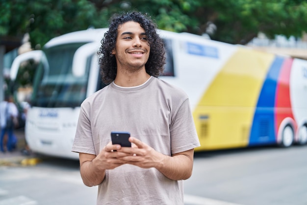 Foto grátis jovem latino sorrindo confiante usando smartphone na rodoviária