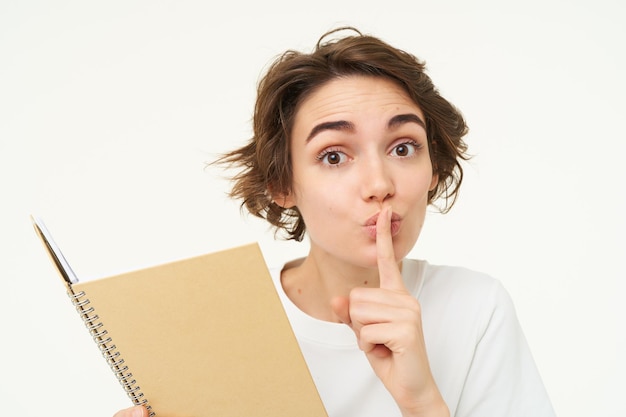 Foto grátis jovem lê seu diário e faz shhh calar a cara, pressionar o dedo nos lábios, escondendo algo pedindo para