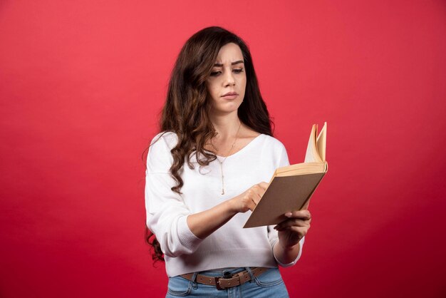 Jovem lendo um livro interessante sobre um fundo vermelho. Foto de alta qualidade