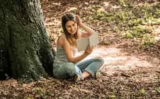 Foto grátis jovem lendo um livro perto de uma árvore
