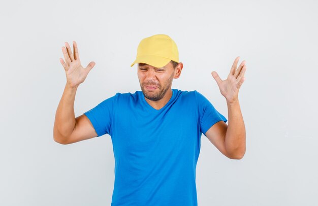 Jovem levantando as mãos em um gesto de impotência em uma camiseta azul