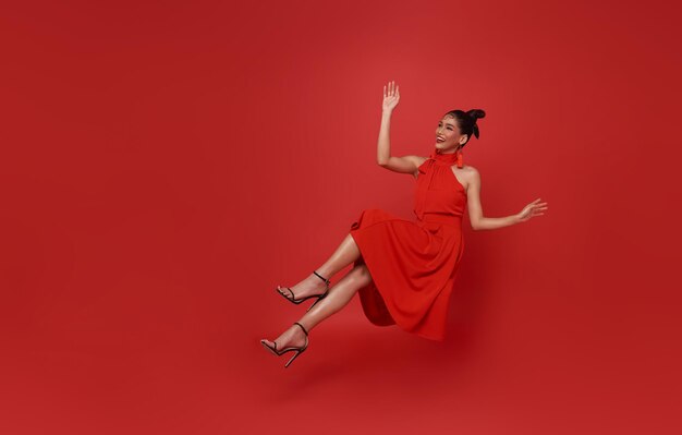 Jovem linda asiática sorridente vestido vermelho flutuando no ar relaxando isolado em fundo vermelho