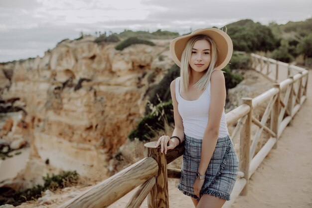 Jovem linda com chapéu de palha em pé no mirante da costa do mar com praia de pedras