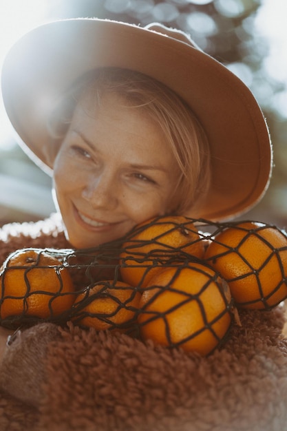 Foto grátis jovem linda de chapéu em um parque de outono, um saco de cordas com laranjas, uma mulher vomita folhas de outono. clima de outono, cores brilhantes da natureza.