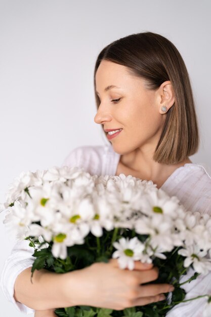 Jovem linda e linda mulher sorridente com um buquê de flores frescas brancas no fundo da parede branca