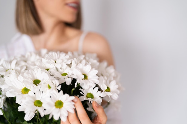 Jovem linda e linda mulher sorridente com um buquê de flores frescas brancas no fundo da parede branca