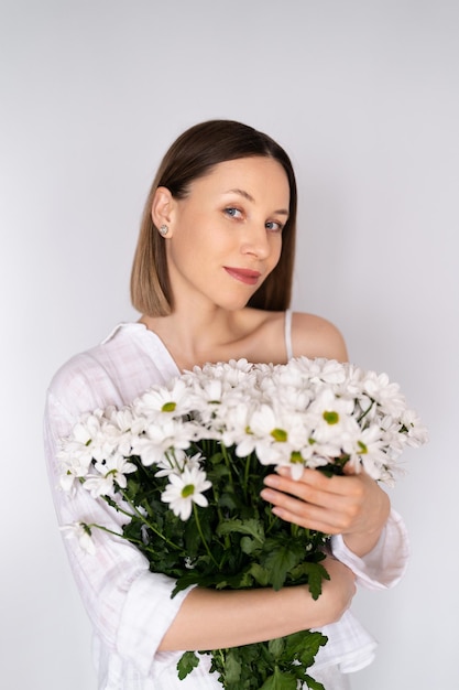 Jovem linda e linda mulher sorridente com um buquê de flores frescas brancas no fundo da parede branca