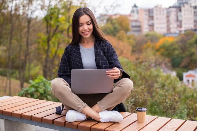 Foto grátis jovem linda e sorridente mulher casual trabalhando no laptop no parque da cidade