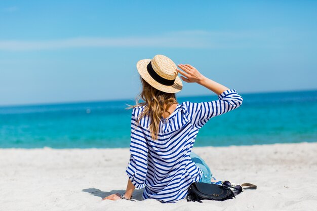 Jovem linda loira bronzeada jovem em pé na praia perto do mar de volta esperando e sonhando com