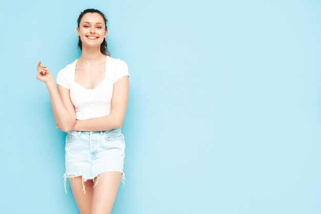 Jovem linda mulher sorridente na saia jeans da moda verão e roupas de cima Mulher despreocupada sexy posando perto da parede azul no estúdio Modelo morena positiva se divertindoAlegre e feliz