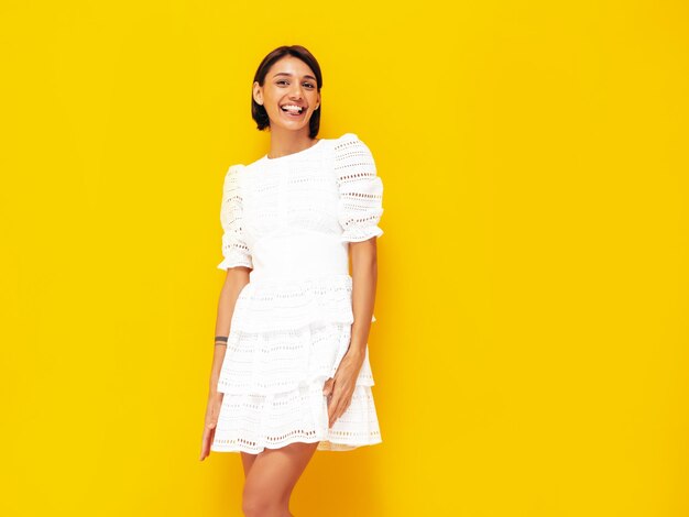 Jovem linda mulher sorridente no vestido branco de verão na moda Mulher despreocupada sexy posando perto da parede amarela no estúdio Modelo positivo se divertindo Alegre e feliz Isolado