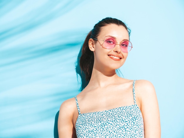 Jovem linda mulher sorridente no vestido de verão da moda mulher despreocupada sexy posando perto da parede azul no estúdio modelo morena positiva se divertindoalegre e feliz isolado