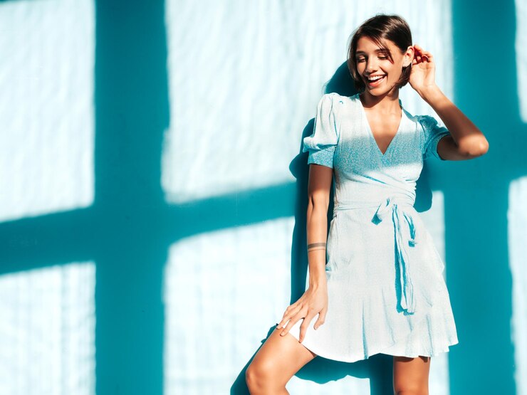 Foto grátis jovem linda mulher sorridente no vestido de verão na moda mulher despreocupada sexy posando perto da parede azul no estúdio modelo positivo se divertindo alegre e feliz no dia ensolarado sombra da janela