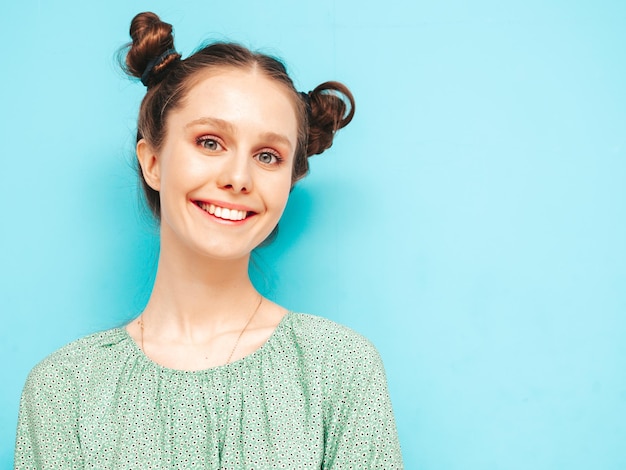 Jovem linda mulher sorridente no vestido verde de verão na moda Mulher despreocupada sexy com penteado de dois chifres posando perto da parede azul no estúdio Modelo positivo se divertindo Alegre e feliz