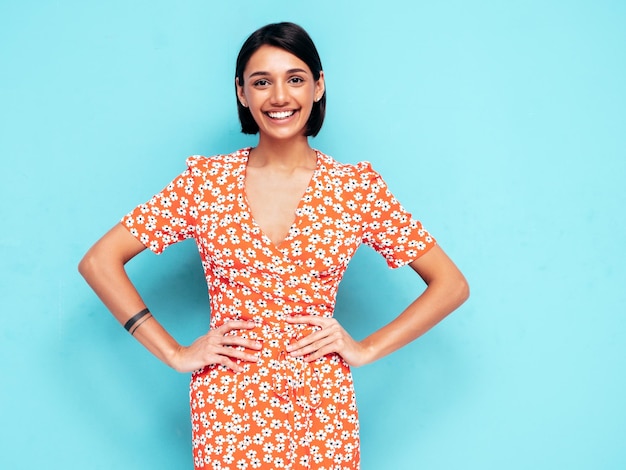 Jovem linda mulher sorridente no vestido vermelho moderno de verão Mulher despreocupada sexy posando perto da parede azul no estúdio Modelo positivo se divertindo Alegre e feliz isolado