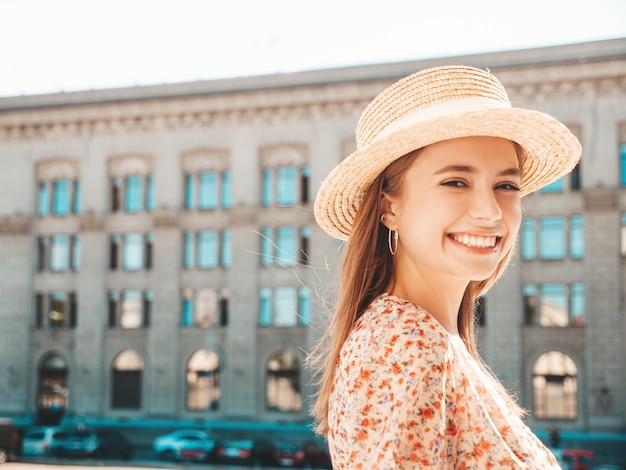 Jovem linda sorridente hipster em vestido de verão na moda Mulher despreocupada sexy posando no fundo da rua com chapéu ao pôr do sol Modelo positivo rindo ao ar livre Alegre e feliz