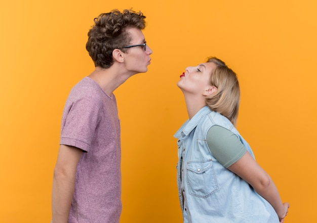 Foto grátis jovem lindo casal, homem e mulher, felizes e apaixonados, mantendo os lábios e se beijando em pé sobre a parede laranja
