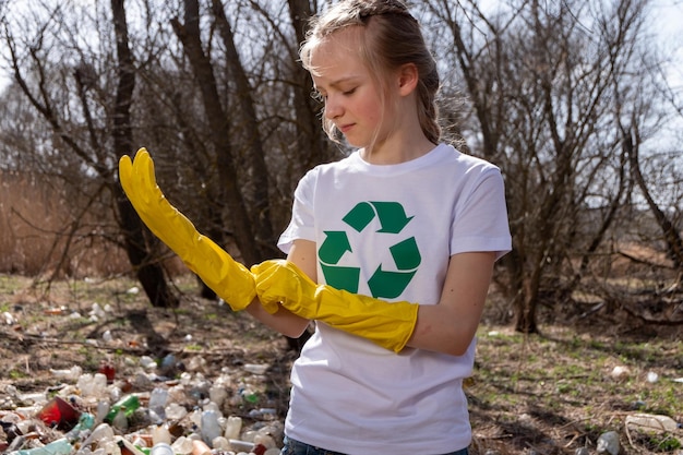 Jovem loira branca caucasiana com um símbolo de reciclagem em sua camiseta colocando luvas amarelas