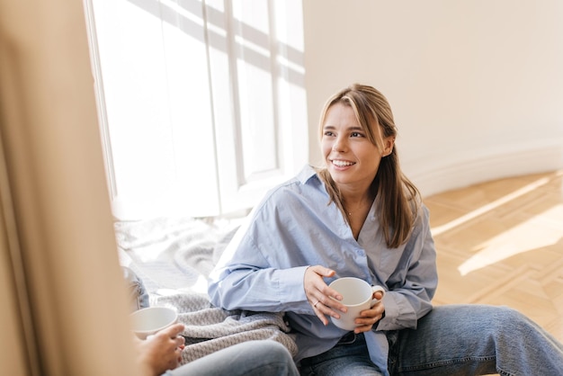 Foto grátis jovem loira caucasiana de camisa e jeans senta-se pela janela e conversa com um amigo. conceito de descanso e recuperação.